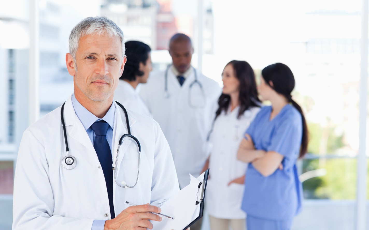 One doctor standing apart from four other doctors discussing information.